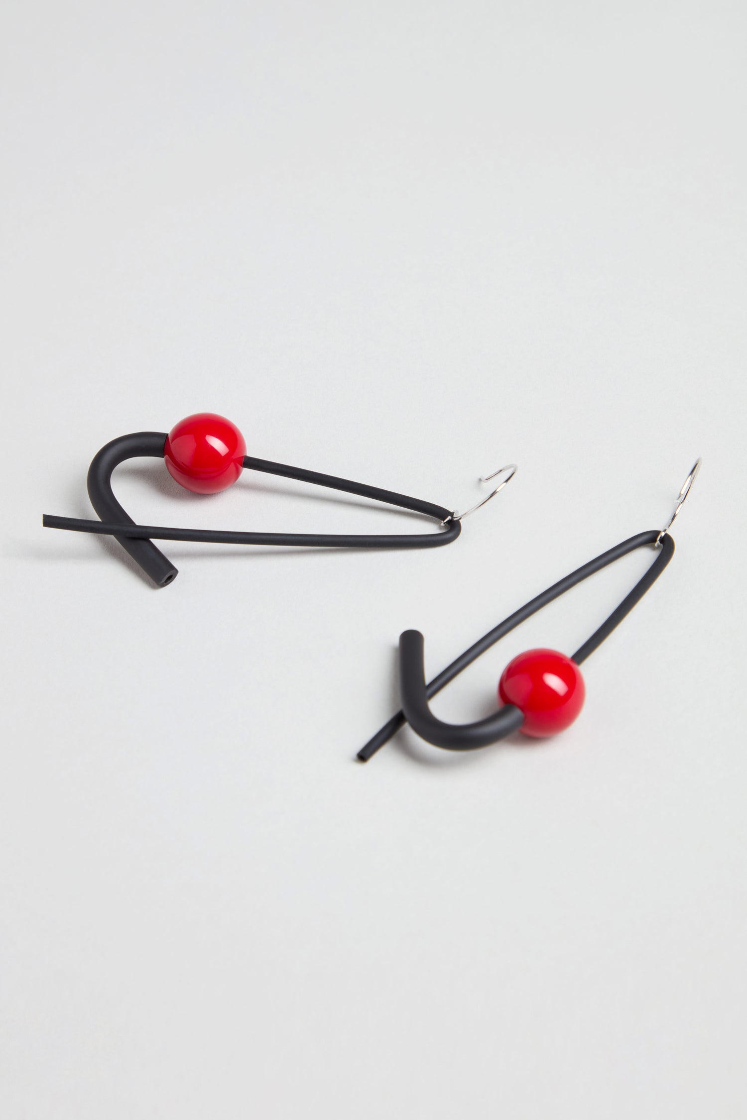 The Sphere Earrings are handmade in Paris, featuring sculptural geometric shapes crafted from black metal wire and accented with a vibrant red spherical bead.