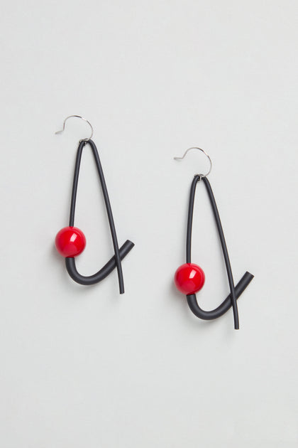 Sphere Earrings: Modern sculptural earrings handmade in Paris, each featuring black curved wire and a red spherical bead, displayed on a light background.