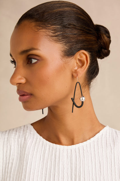 Woman with hair in a bun wearing a white textured top and the Sphere Earrings—large, abstract black contemporary earrings featuring a silver bead—shown in profile against a neutral background.