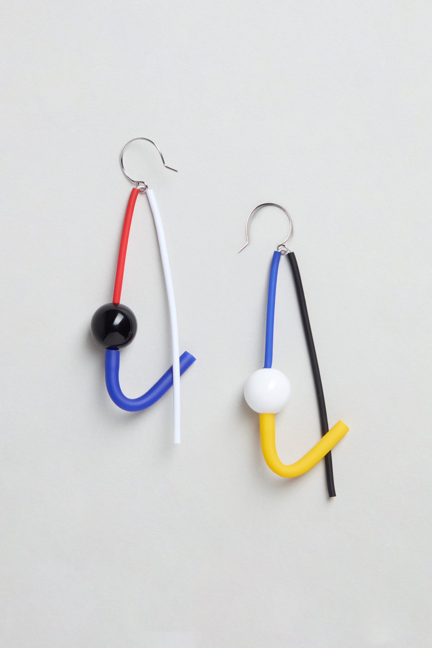 The Kandinsky Sphere Earrings feature bent tubes in red, blue, white, yellow, and black with round beads. Handmade in Paris, these abstract sculptural earrings are showcased on a light background.
