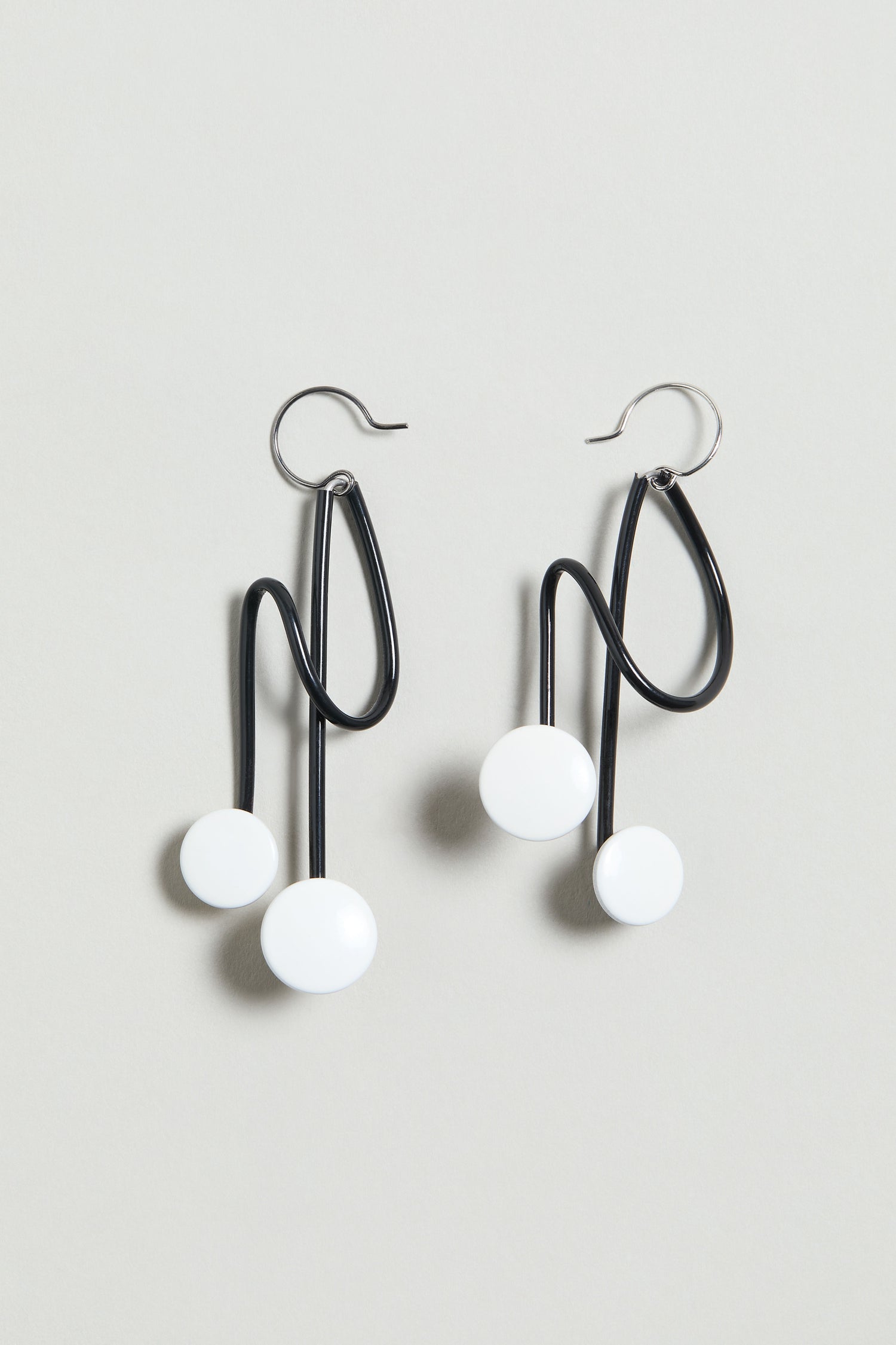 The Symphony Earrings are black wire statement pieces with abstract wavy shapes and two white circular accents each, shown on a light gray background—an ideal choice for contemporary jewellery lovers.