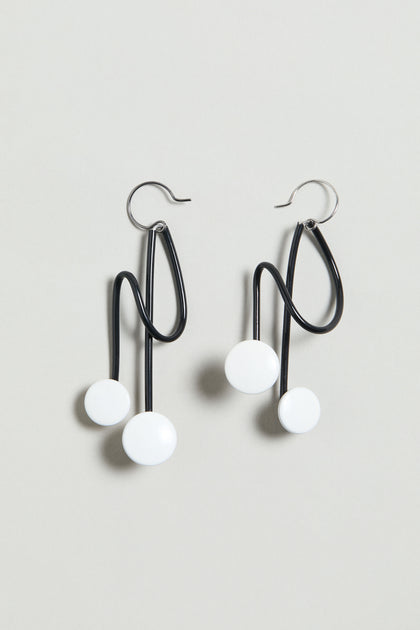 The Symphony Earrings are black wire statement pieces with abstract wavy shapes and two white circular accents each, shown on a light gray background—an ideal choice for contemporary jewellery lovers.