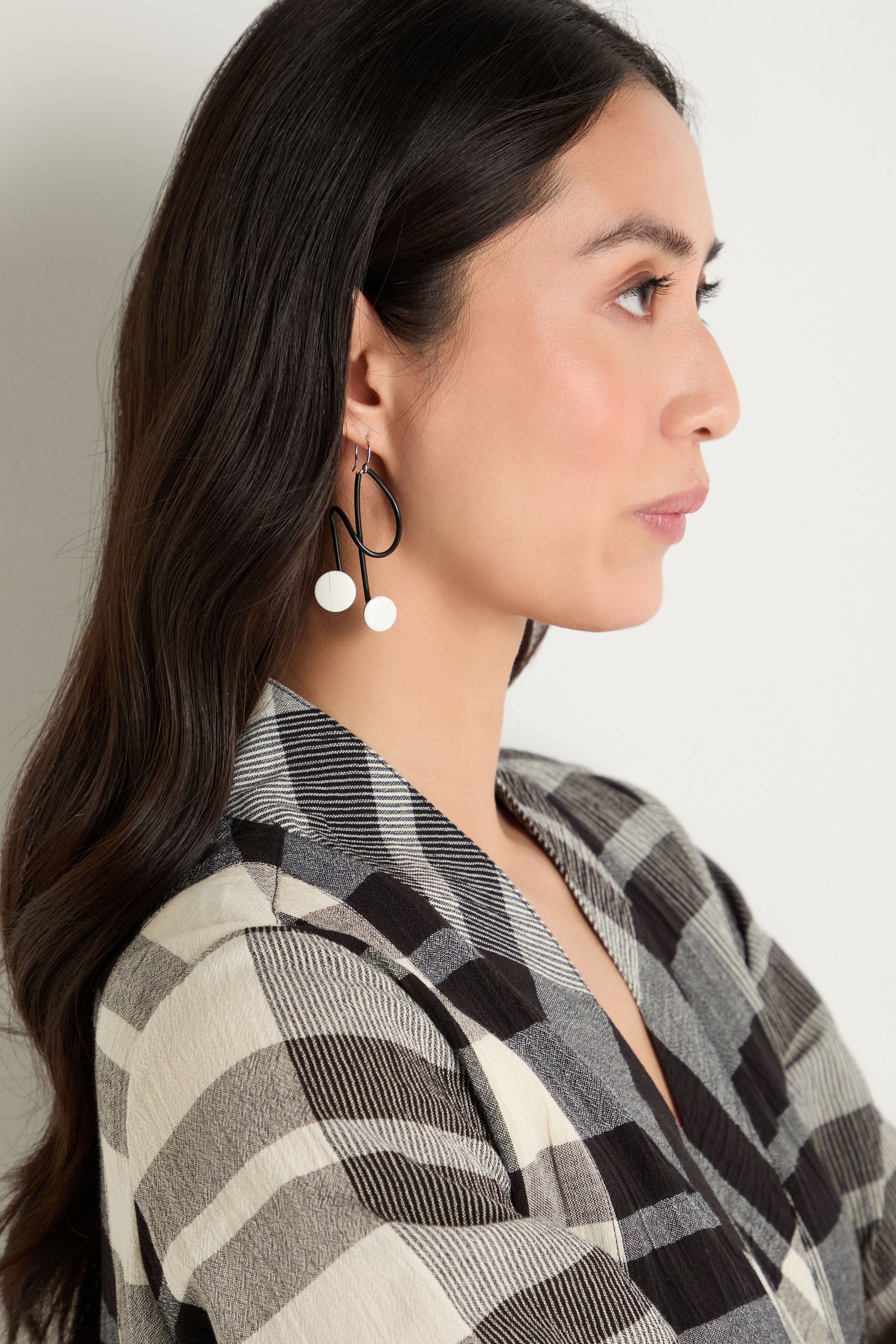 Woman in profile wearing a black and white plaid blazer and the Symphony Earrings—large, abstract statement earrings with white circular accents that are an eye-catching piece of contemporary jewellery.