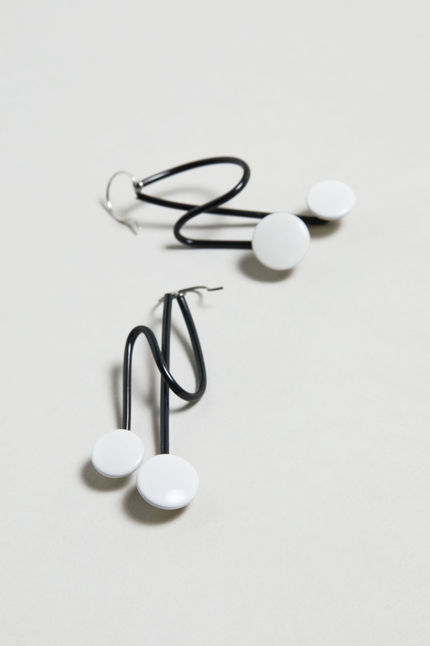 The Symphony Earrings feature black zigzag metal stems and round white disc accents, making them perfect for modern jewelry lovers. Displayed on a plain background.