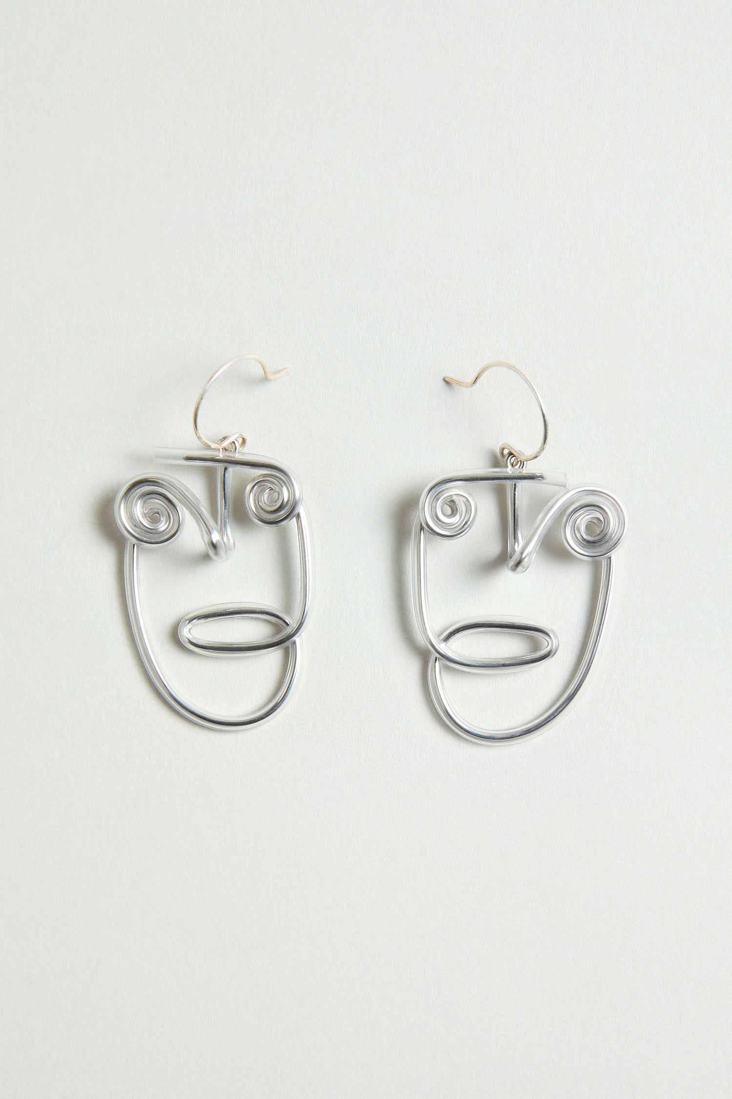 The Mini Faces Earrings are silver, abstract human face earrings with spiral eyes and minimalist features, showcasing sculptural design against a plain light background.