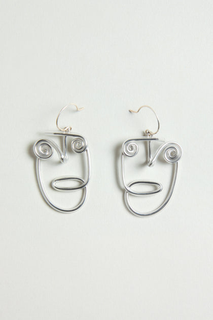 The Mini Faces Earrings are silver, abstract human face earrings with spiral eyes and minimalist features, showcasing sculptural design against a plain light background.