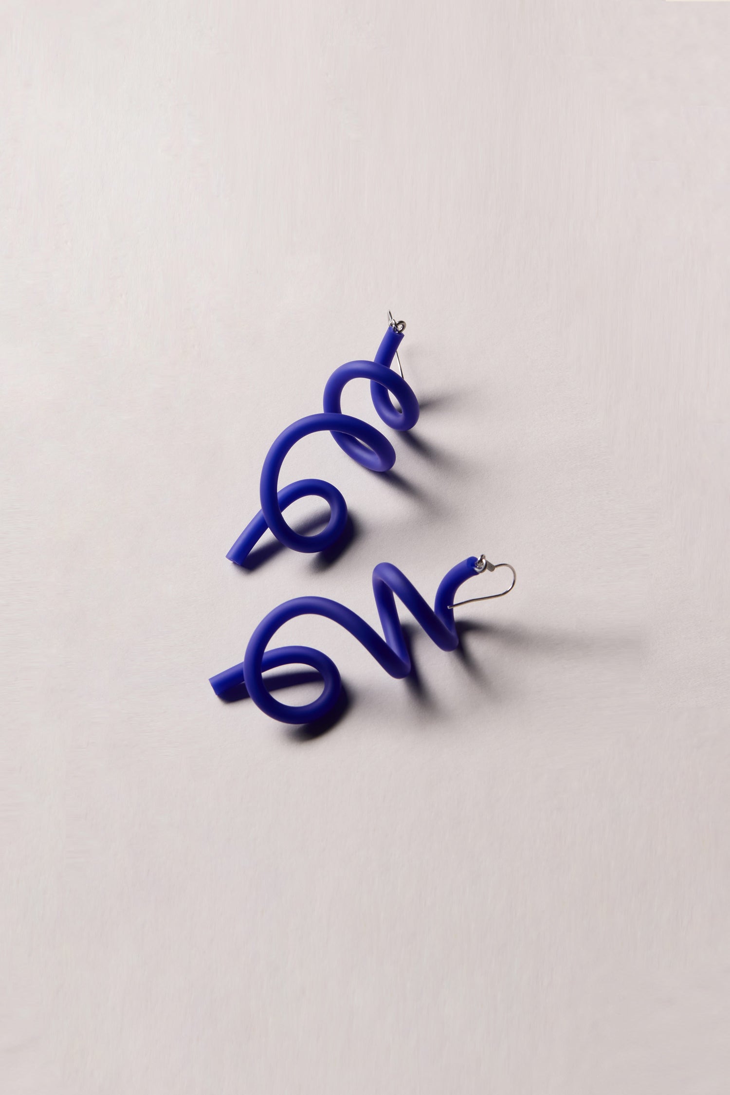 A pair of the Sketch Earrings, showcasing chunky, sculpted blue designs with hook fastenings, laid on a light-colored surface; unique contemporary jewelry at its finest.