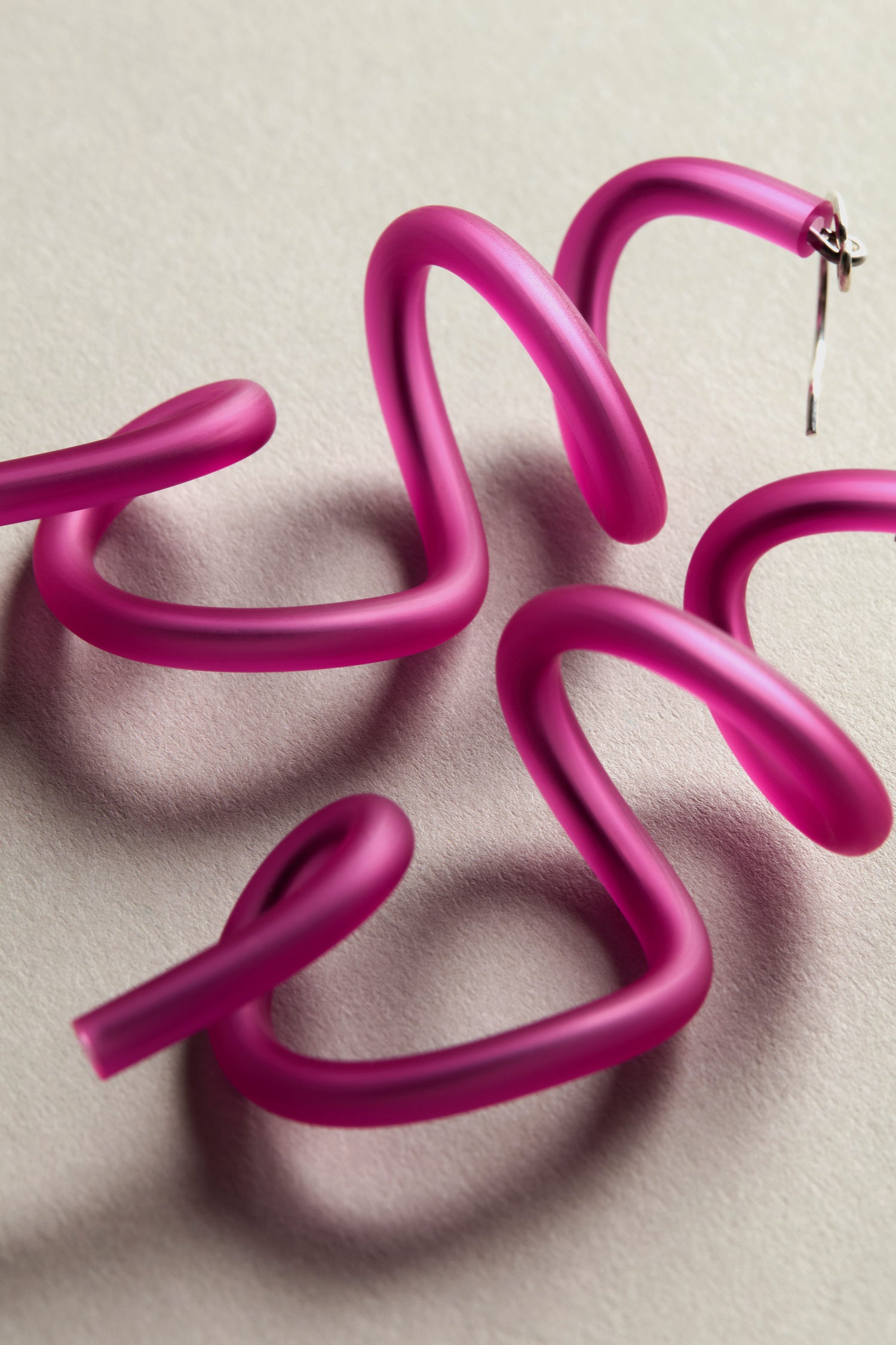 Sketch Earrings, twisty and pink with a modern art vibe, are arranged on a light surface.
