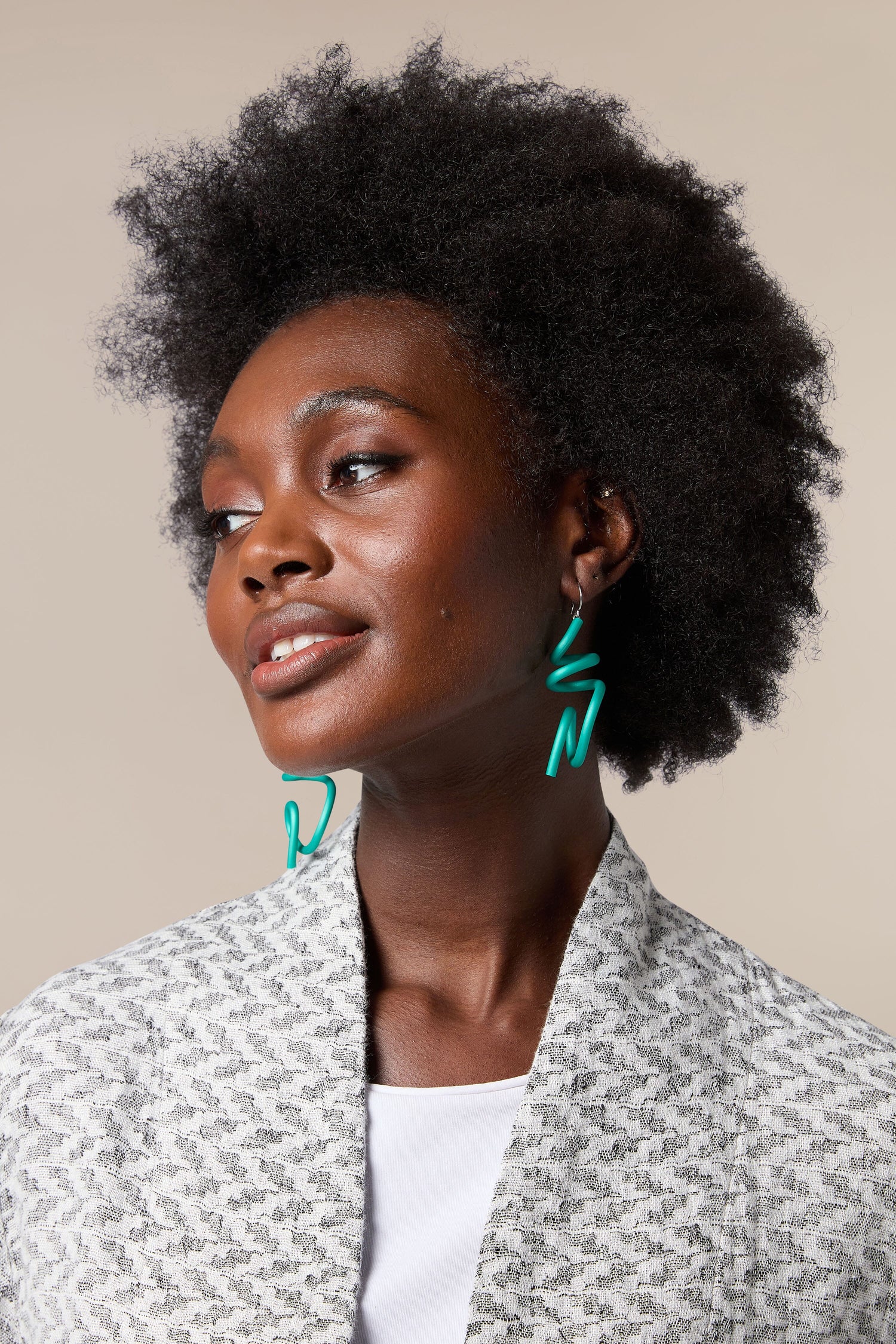 A woman with afro hair wearing a grey jacket and Sketch Earrings.