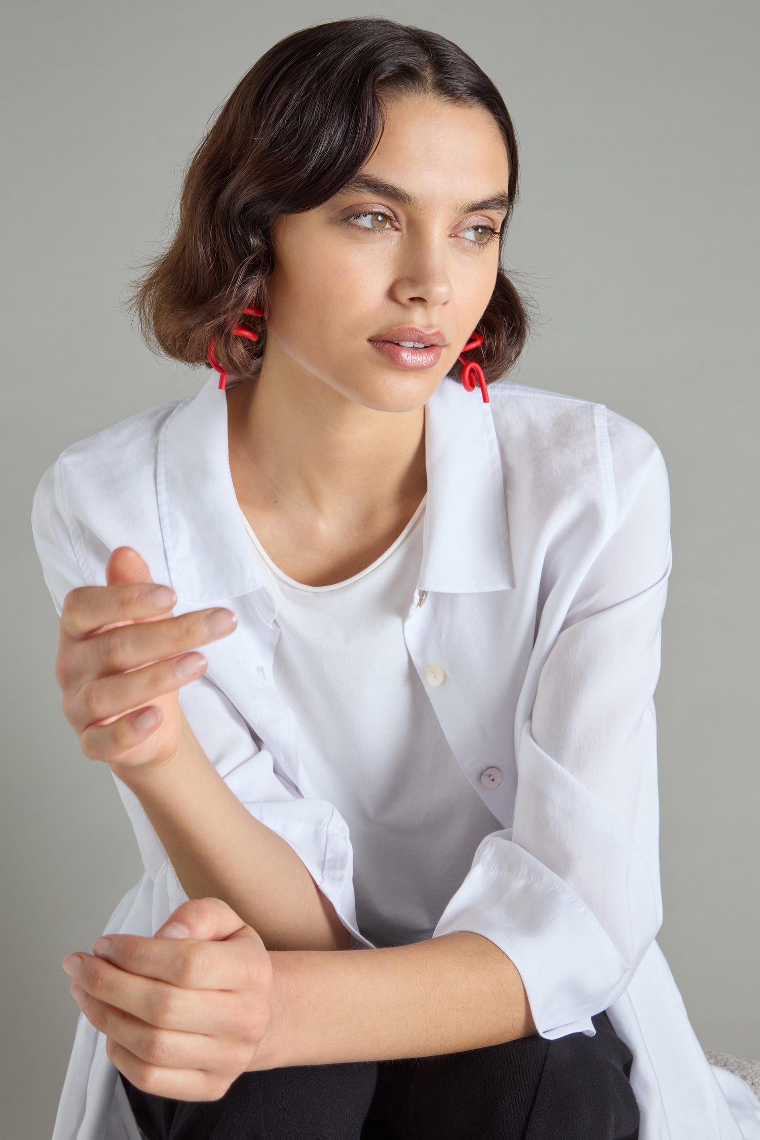 A person with short brown hair in a white shirt and striking Sketch Earrings sits against a neutral background.