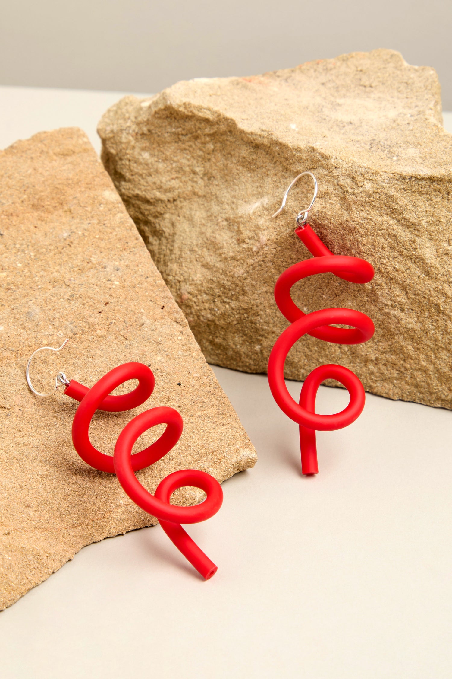 The red spiral Sketch Earrings beautifully showcase their contemporary design on coarse stone slabs.