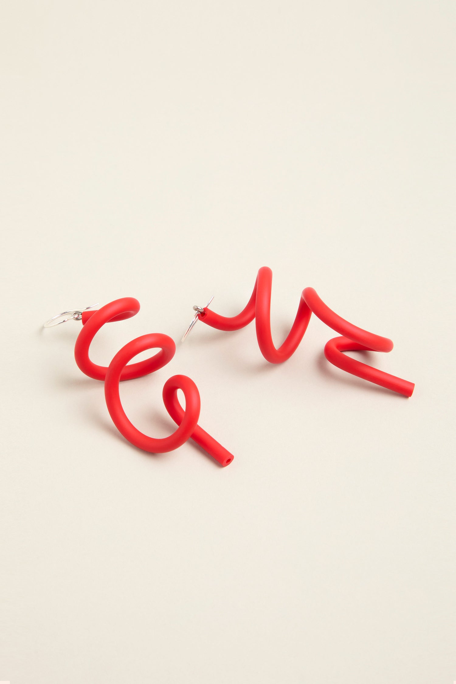 Two sketch earrings, colored in red squiggles, are set against a simple light background, highlighting their contemporary design.