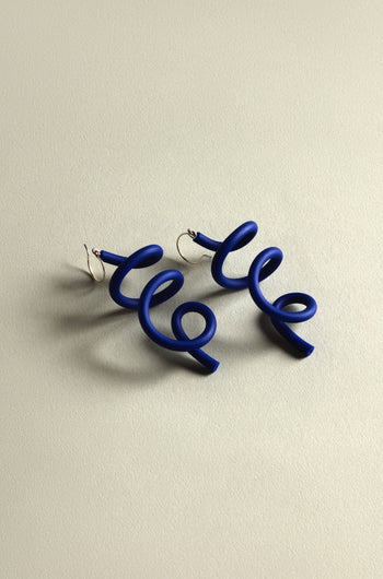 Sketch Earrings with a curling blue wire design elegantly rest on a light beige background, showcasing their contemporary and modern art flair.