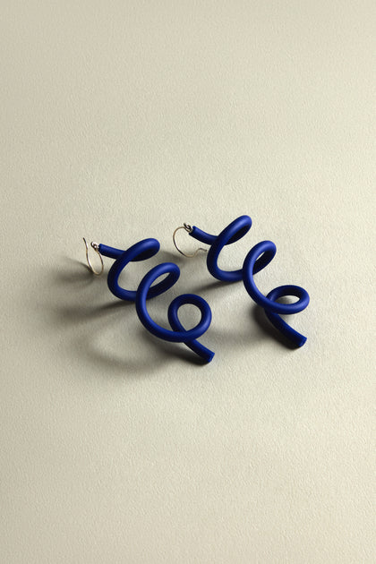 Sketch Earrings with a curling blue wire design elegantly rest on a light beige background, showcasing their contemporary and modern art flair.