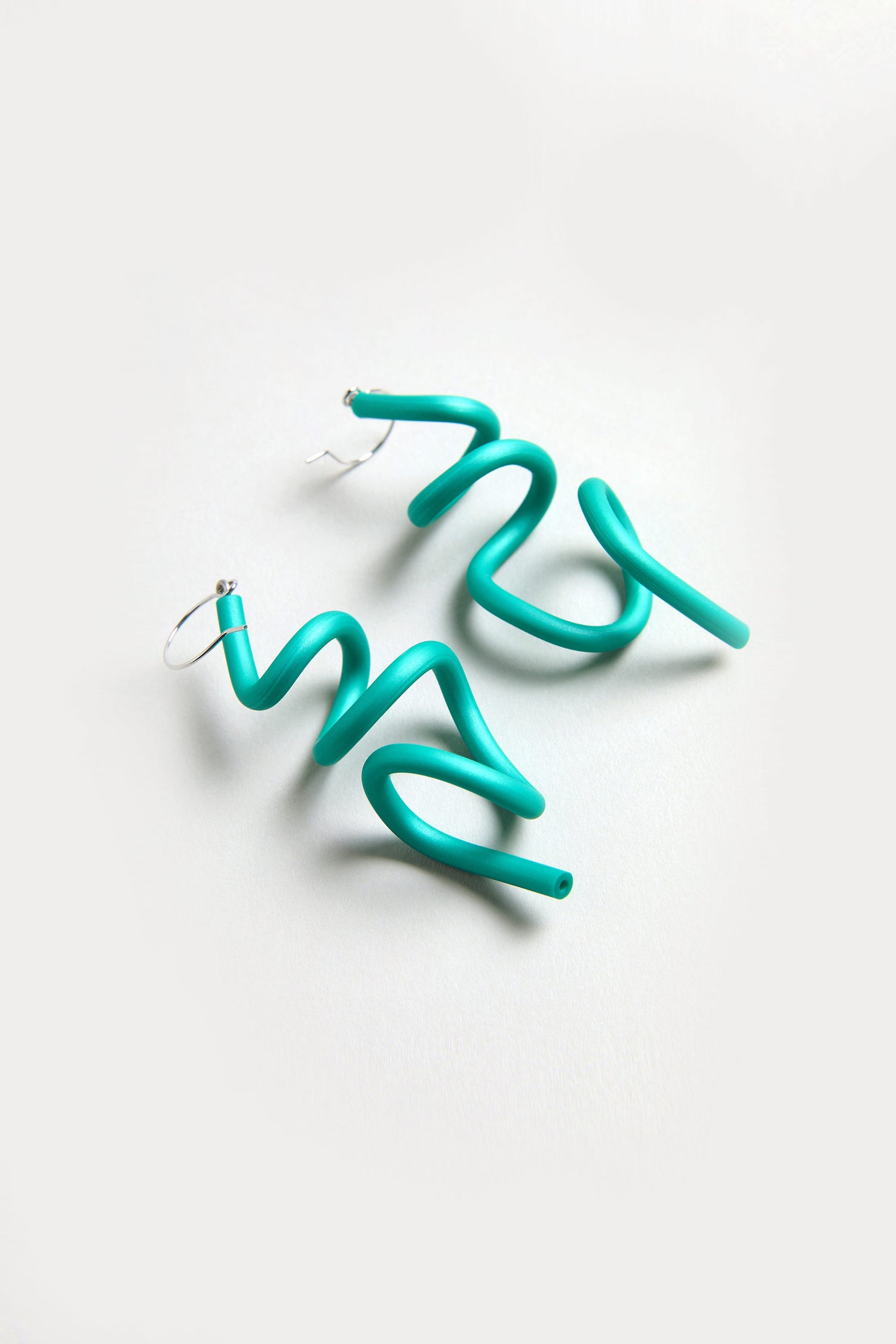 A pair of bright turquoise Sketch Earrings in a spiral shape with hoop fastenings, displayed on a light background.