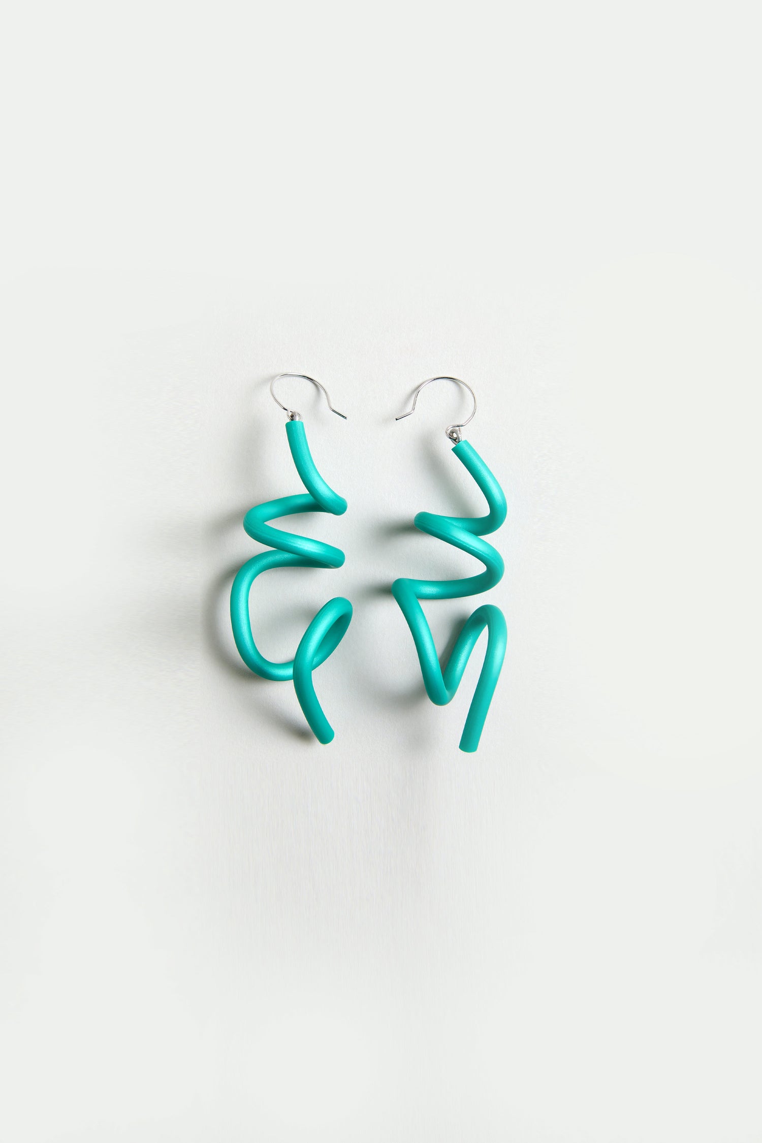 The Sketch Earrings feature sculptural, irregular squiggly turquoise shapes with silver hooks, displayed on a plain white background.