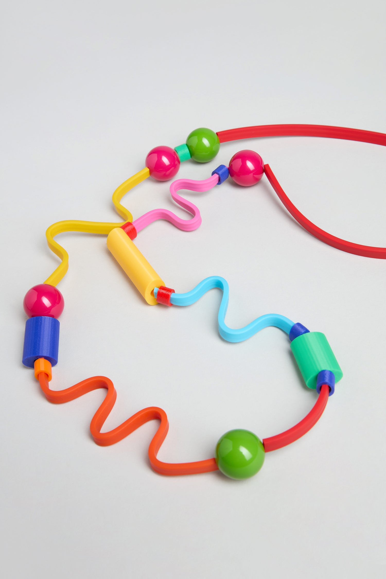 The Rainbow Graphic Pop Necklace features large, colorful beads in various shapes on wavy, curved wires—resembling playful sculptural jewelry, handmade in Paris style and inspired by a bead maze toy.