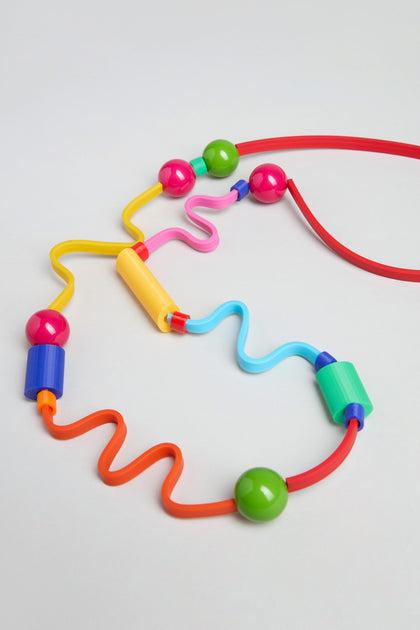 The Rainbow Graphic Pop Necklace features large, colorful beads in various shapes on wavy, curved wires—resembling playful sculptural jewelry, handmade in Paris style and inspired by a bead maze toy.
