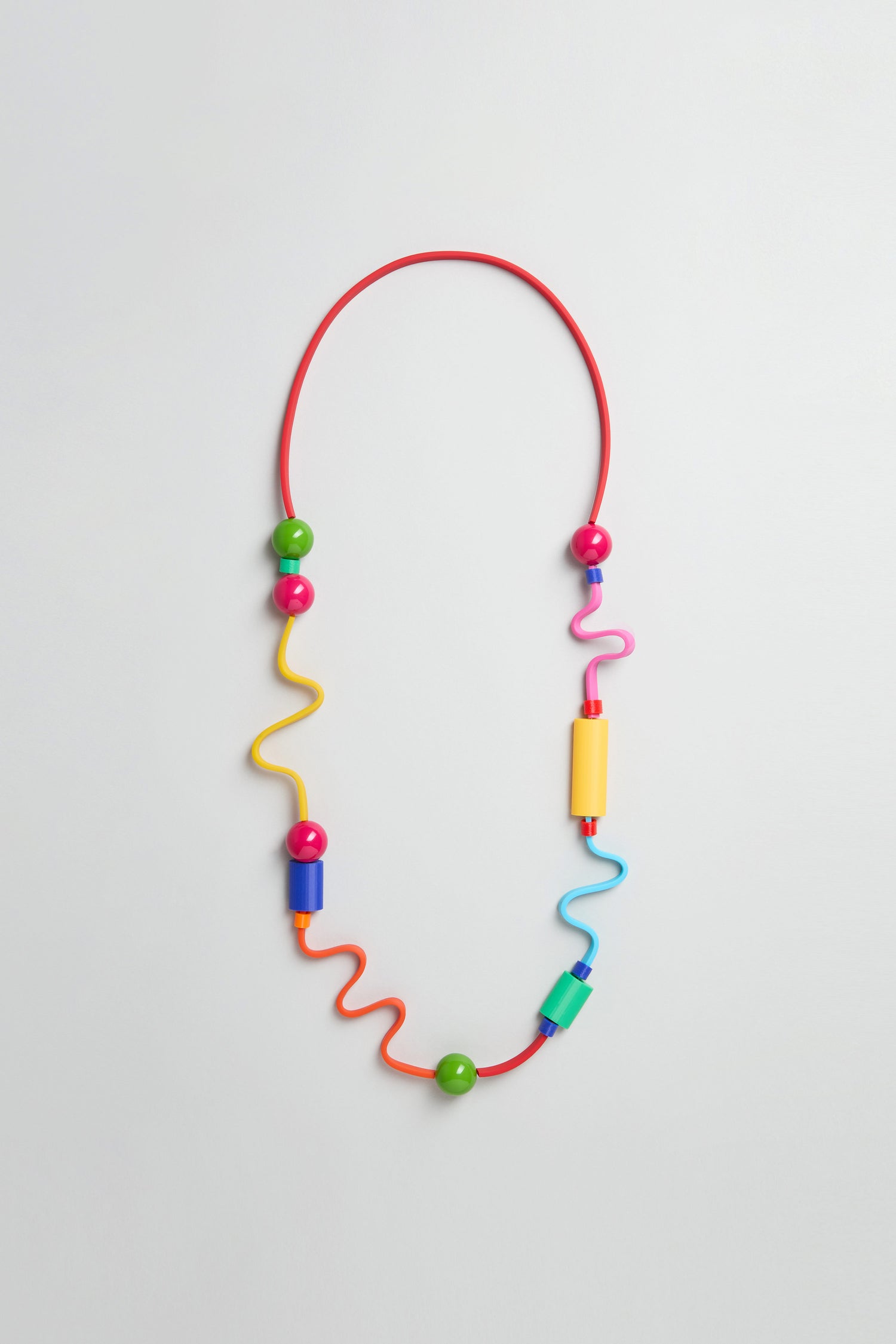 The Rainbow Graphic Pop Necklace is a sculptural piece with a red flexible band, colorful wavy segments, and large green, yellow, pink, and blue beads—handmade in Paris and shown on a plain light background.