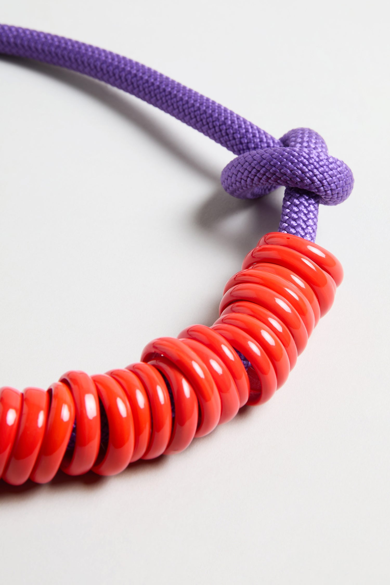 A close-up of the Murano Glass Rings Necklace, showcasing a purple textured rope cord tied in a knot with multiple glossy Murano glass rings threaded onto it.