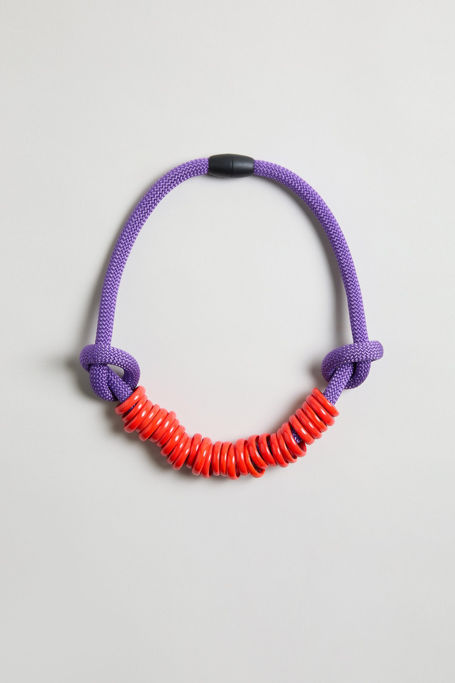 The Murano Glass Rings Necklace features a thick, textured purple rope with two knots and glossy red Murano glass rings grouped at the center.