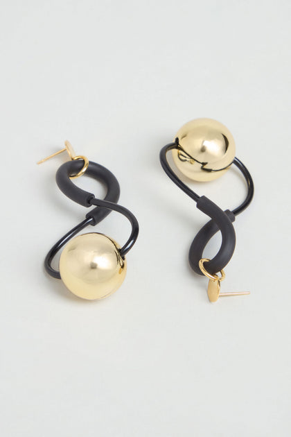 The Infinity Earrings feature gold spheres linked by gracefully curved black loops, presented against a simple light background to highlight their sculptural design.