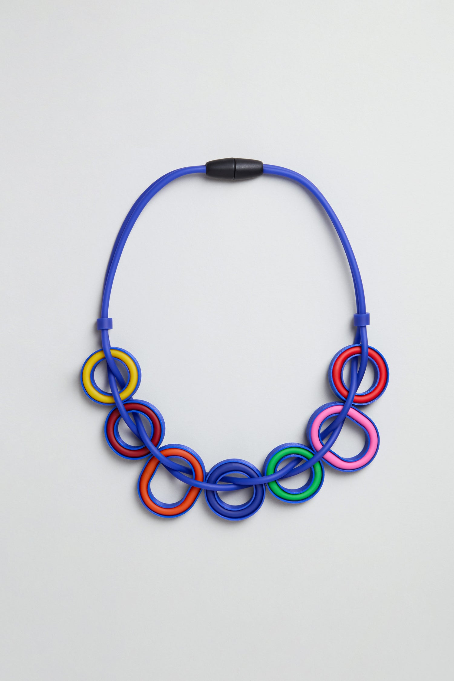 The Colour Pop Rings Necklace, handmade in Paris, features interlocking blue, red, yellow, pink, green, and black rings with a black magnetic clasp—presented on a plain light background.
