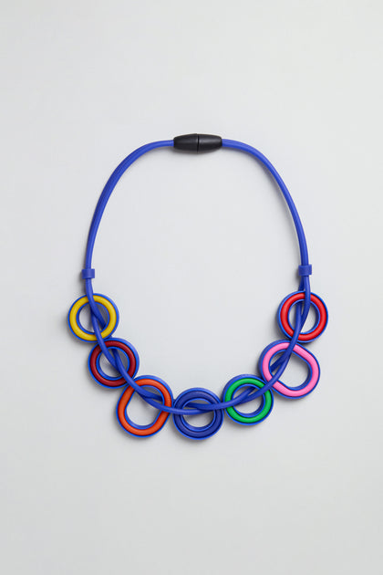 The Colour Pop Rings Necklace, handmade in Paris, features interlocking blue, red, yellow, pink, green, and black rings with a black magnetic clasp—presented on a plain light background.
