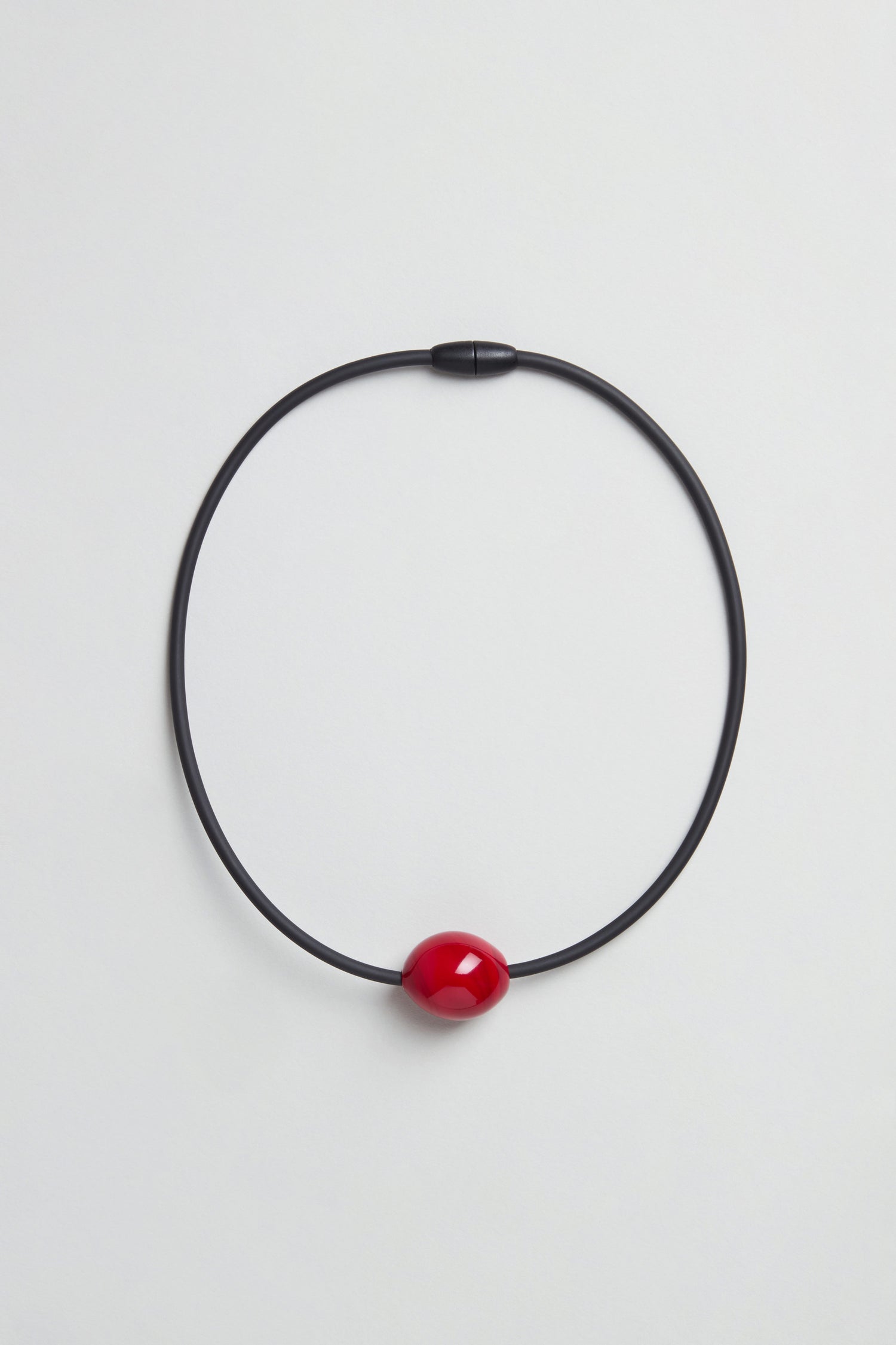 The Murano Bead Necklace is a minimalist piece, handmade in Paris, with a black circular design and a glossy red bead at the center, shown against a plain white background.