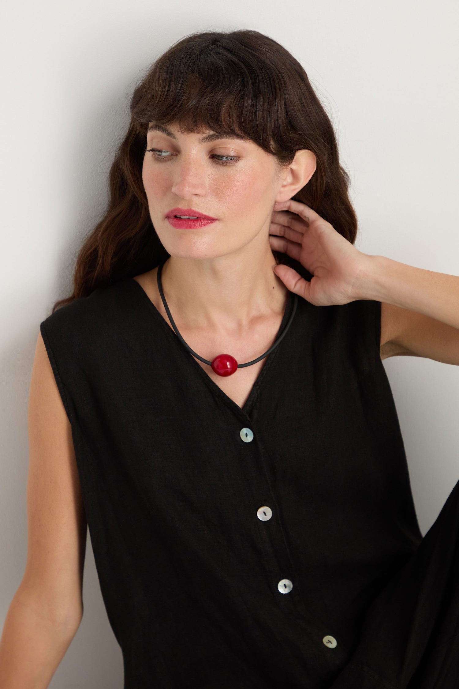 A woman with long brown hair wears a sleeveless black buttoned top and a Murano Bead Necklace, handmade in Paris, as she gazes to the side with one hand gently touching her neck.