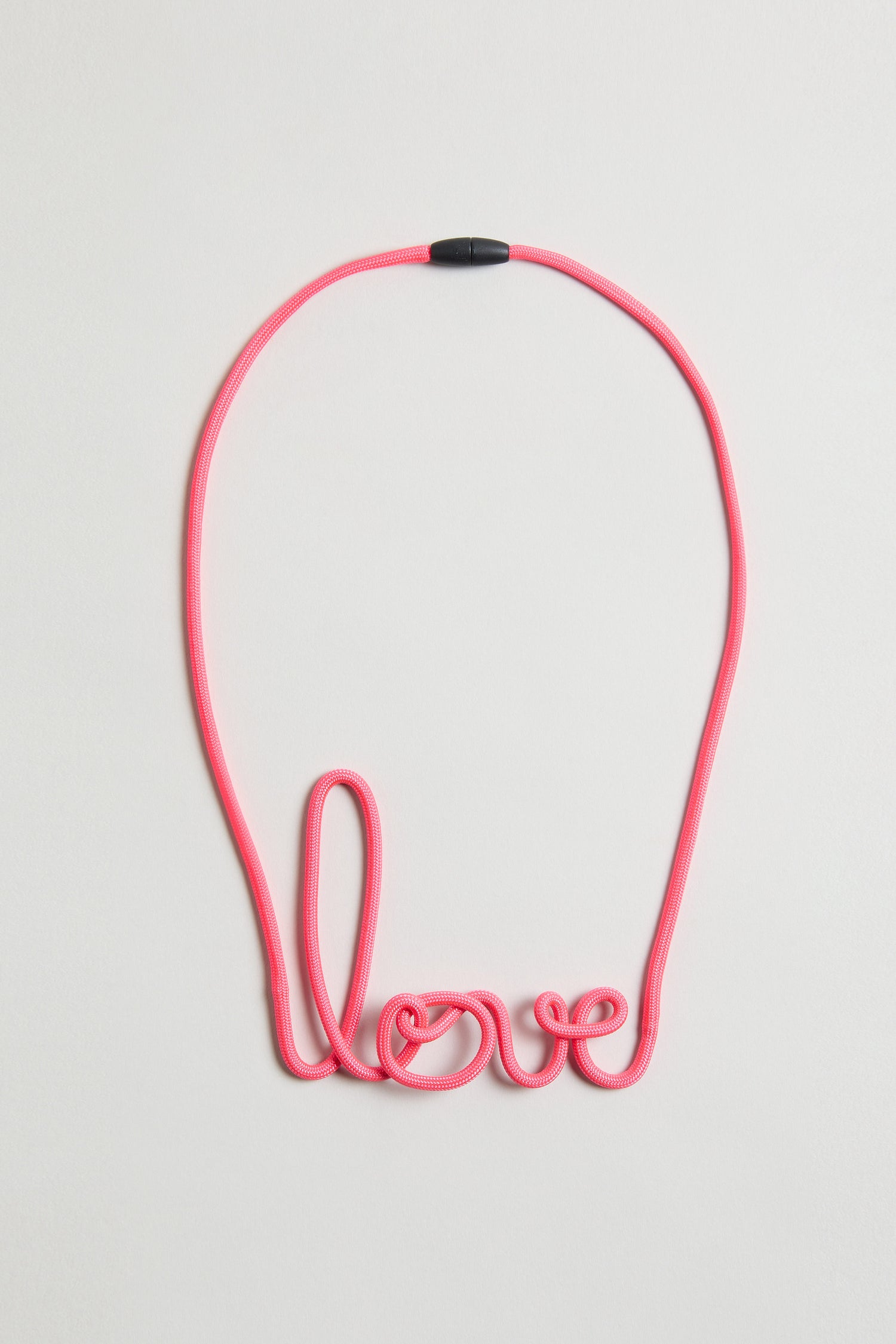 The Love Necklace is a handmade pink cord necklace shaped to spell "love," shown on a simple light background.