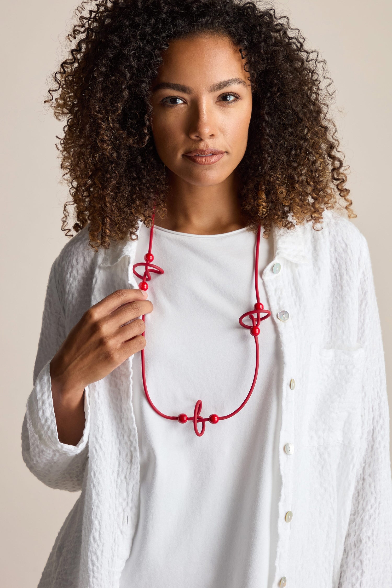 A person with curly hair wearing a white shirt and a bold Trio Squiggle Necklace by Samuel Coraux looks directly at the camera.