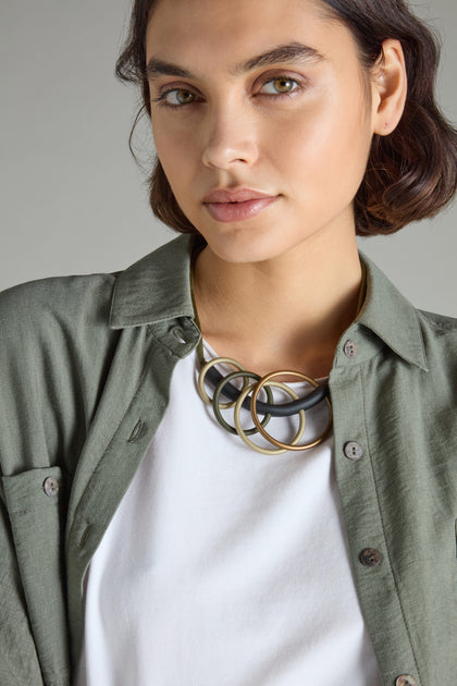 A person sporting a green shirt layered over a white t-shirt is accessorized with the Quadruple Circles Necklace, radiating modern chic.