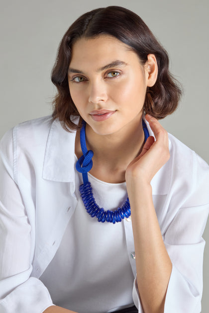 A person with short brown hair is wearing a white shirt and an eye-catching Murano Glass Rings Necklace by Samuel Coraux, posing gracefully against a neutral background.