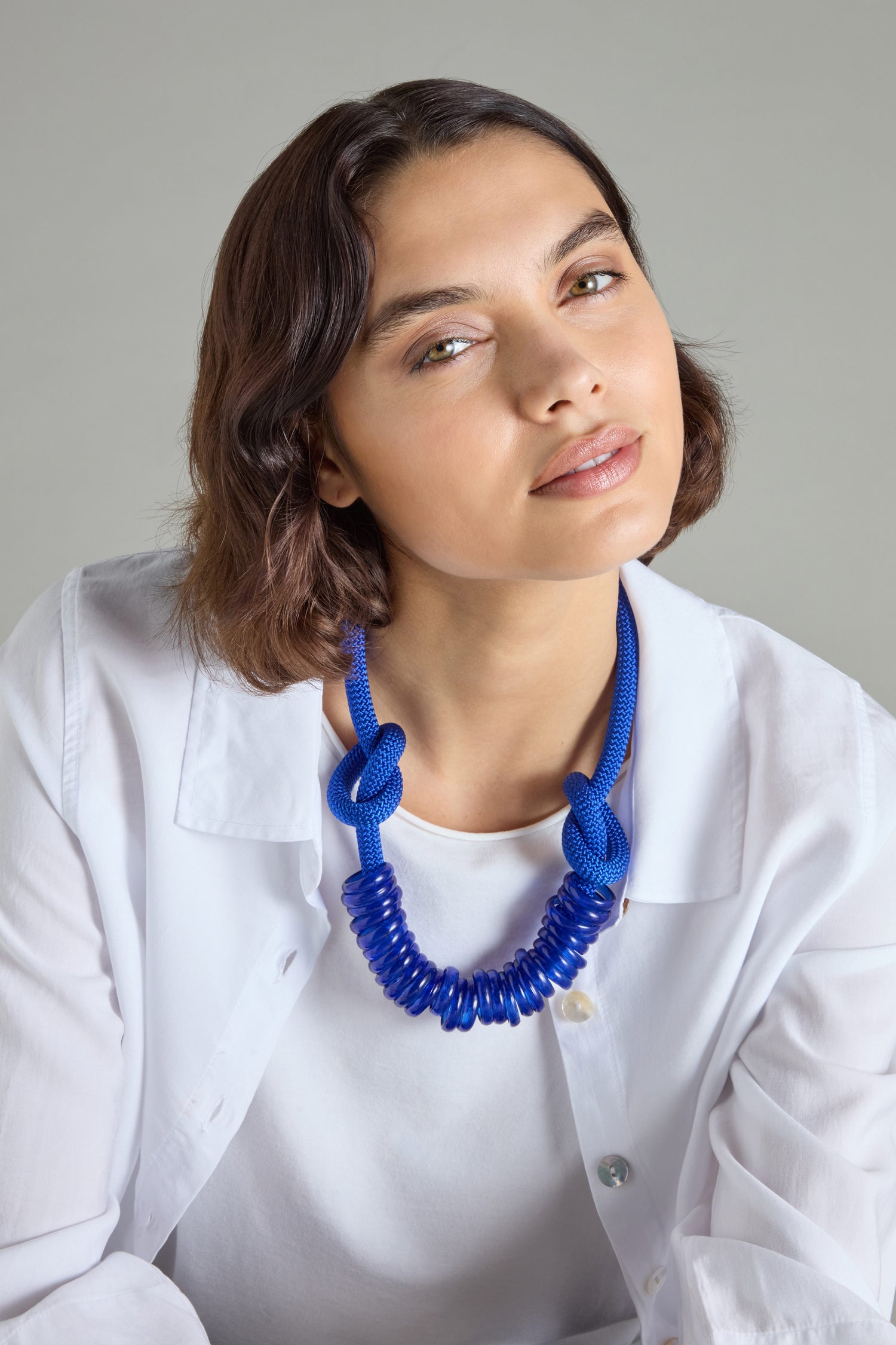 A person wearing a white shirt and the bold, contemporary Murano Glass Rings Necklace by Samuel Coraux gazes slightly upward with a neutral expression, the vibrant design echoing elegance.