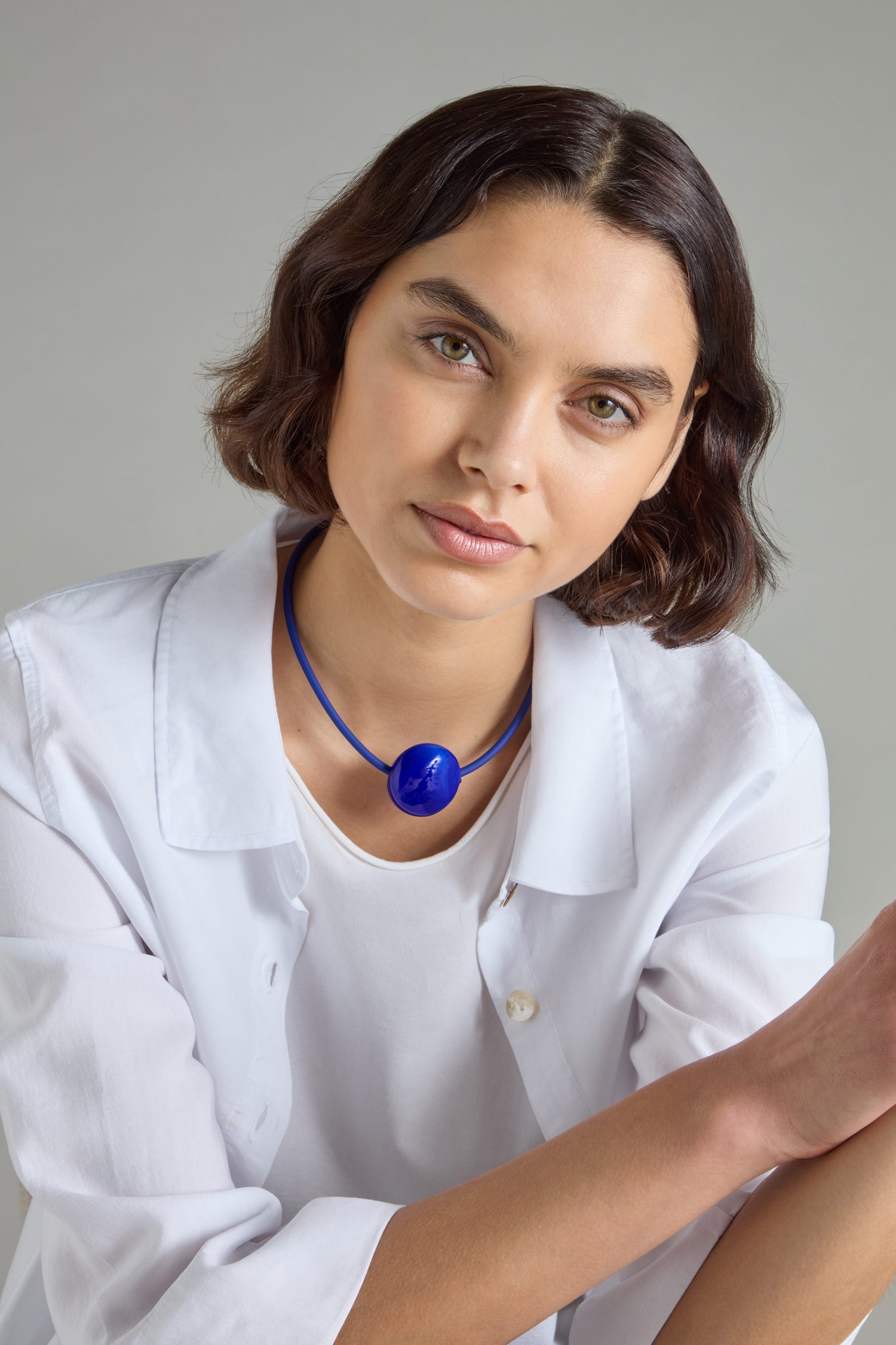 A woman with short brown hair wearing a white shirt is adorned with a striking Murano Glass Pebble Necklace, which is handcrafted in France, as she sits against a plain background.