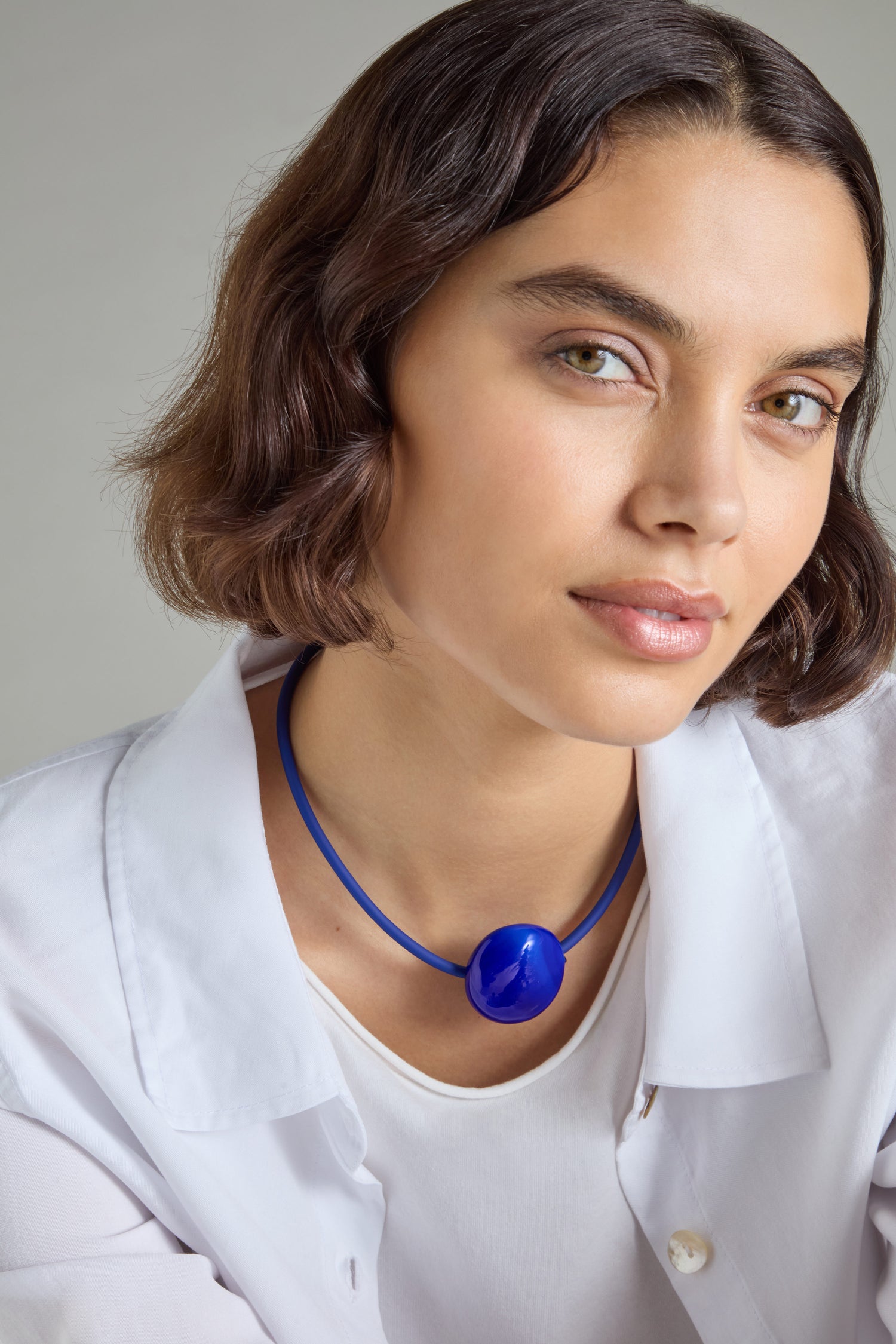 A person with short hair is adorned in a white shirt and wearing a striking handcrafted Murano Glass Pebble Necklace, created by Samuel Coraux in France.