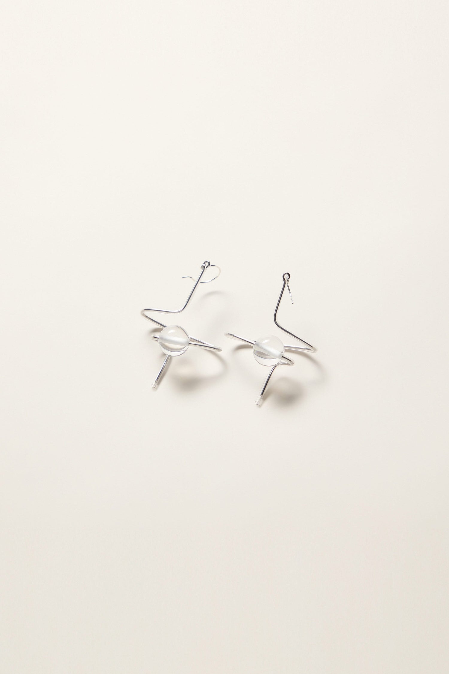 The Sketch Ball Earrings, featuring a sculpted abstract wavy design with white spherical accents, are laid flat on a white surface, showcasing the unique touch of French jewellery by Samuel Coraux.