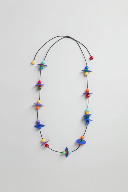 The Orbit Necklace showcases an abstract geometric design with multicolored beads and blue discs on a thin black cord, handmade in Paris.