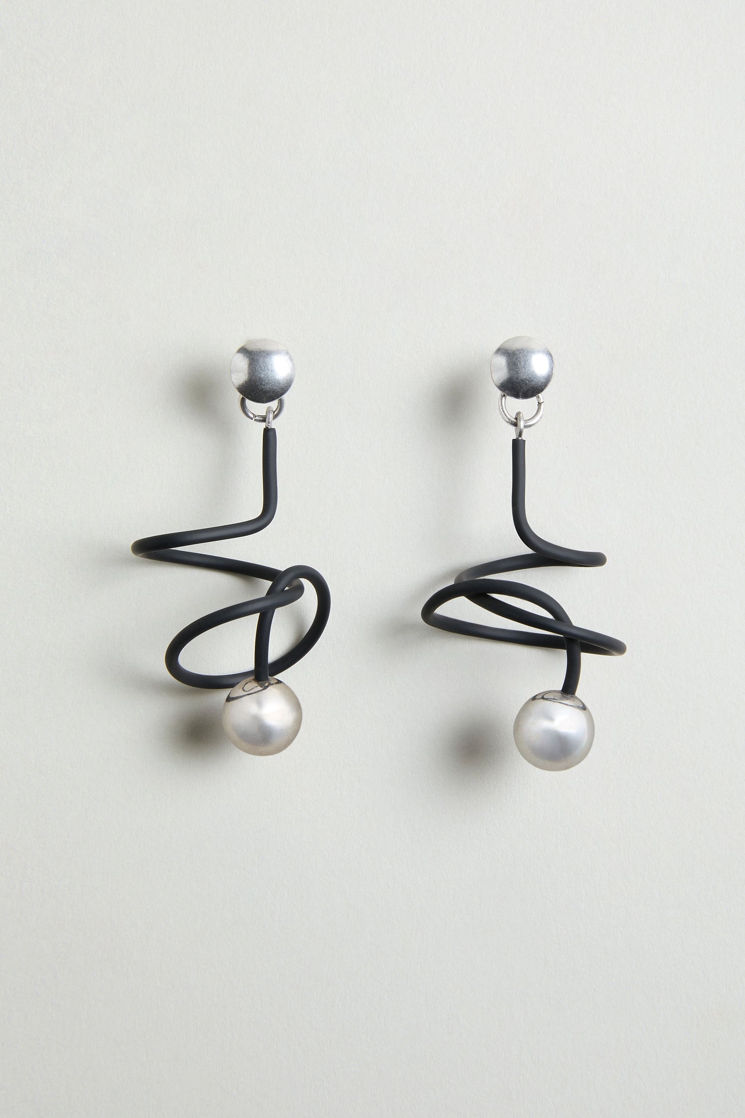 The Graphic Squiggle Earrings feature silver studs, black spiral wire designs, and dangling round white pearls in a statement drop earrings style.
