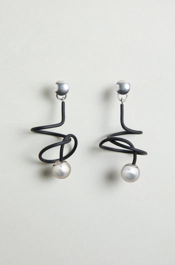 The Graphic Squiggle Earrings feature silver studs, black spiral wire designs, and dangling round white pearls in a statement drop earrings style.