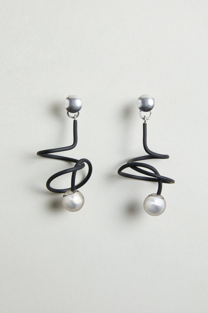 The Graphic Squiggle Earrings feature silver studs, black spiral wire designs, and dangling round white pearls in a statement drop earrings style.
