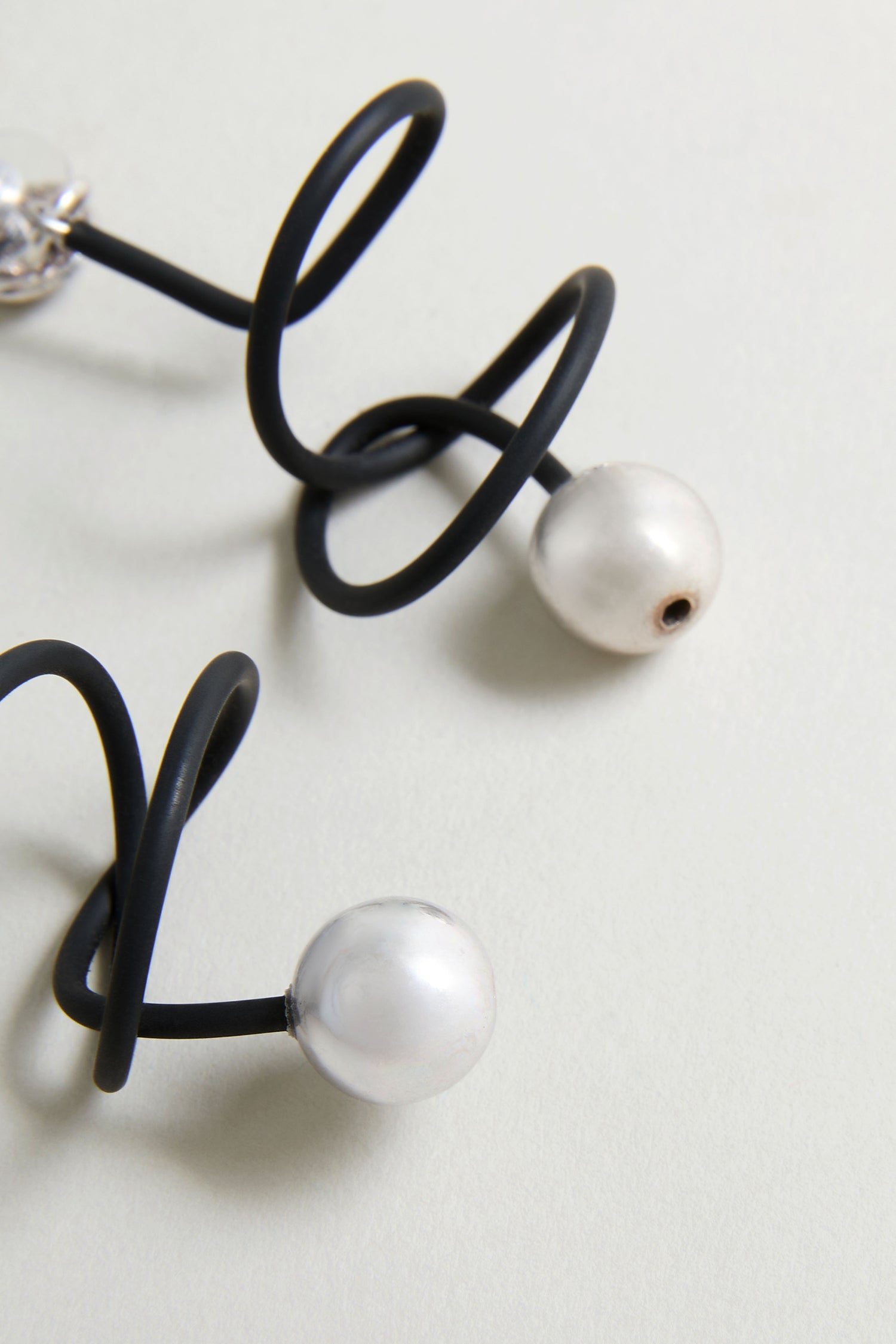 Two black spiral wires from the Graphic Squiggle Earrings each feature a single white pearl bead at the end, displayed on a light surface.