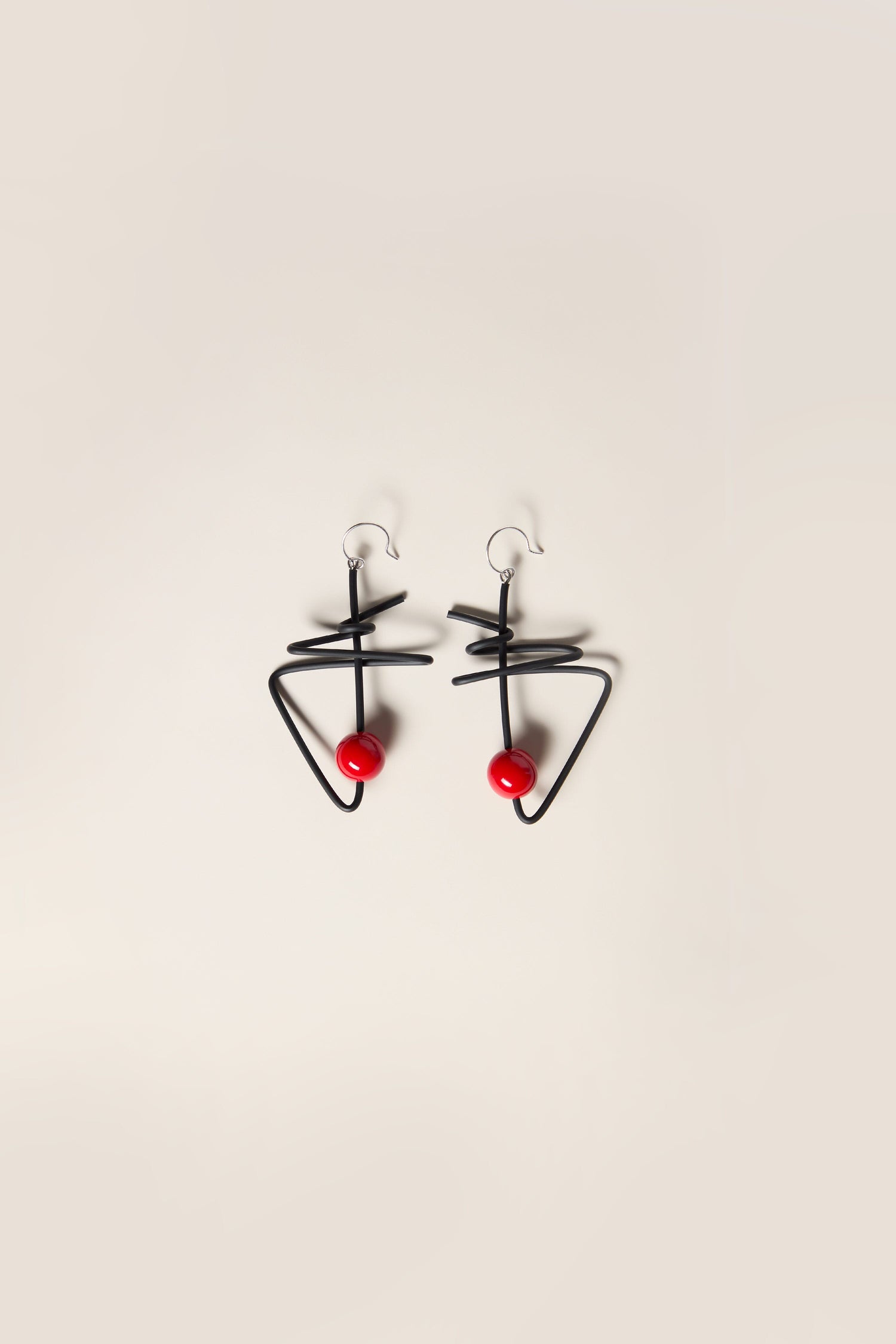 The Doodle Earrings are a remarkable pair of abstract black metal earrings with a geometric design, each adorned with a single red bead. They are exquisitely crafted, showcasing the unique touch characteristic of French jewellery maker Samuel Coraux.