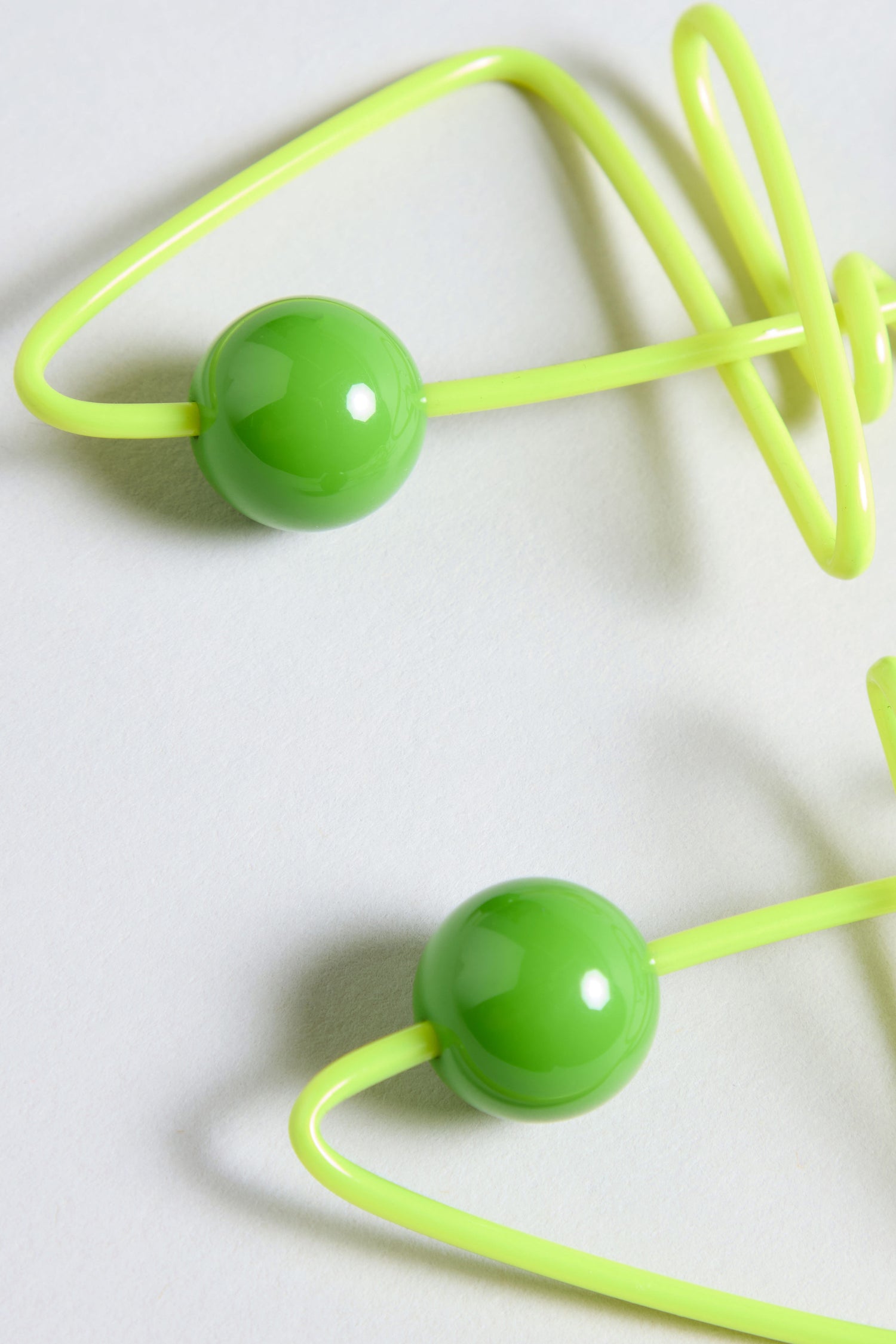 Close-up of two bright green plastic beads threaded onto a yellow flexible cord, featuring the playful French style of Doodle Earrings, placed on a light grey surface.