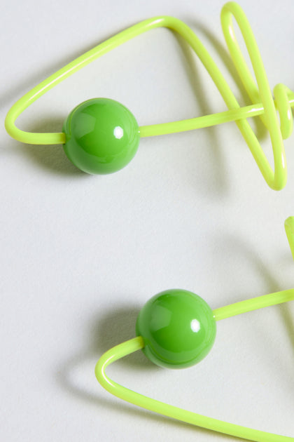 Close-up of two bright green plastic beads threaded onto a yellow flexible cord, featuring the playful French style of Doodle Earrings, placed on a light grey surface.