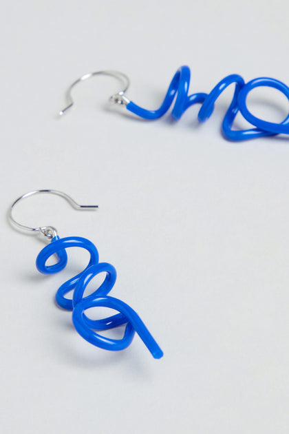 Handmade in Paris, the Mini Sketch Earrings feature blue plastic twisted into spirals with silver hooks and are shown on a simple light background.
