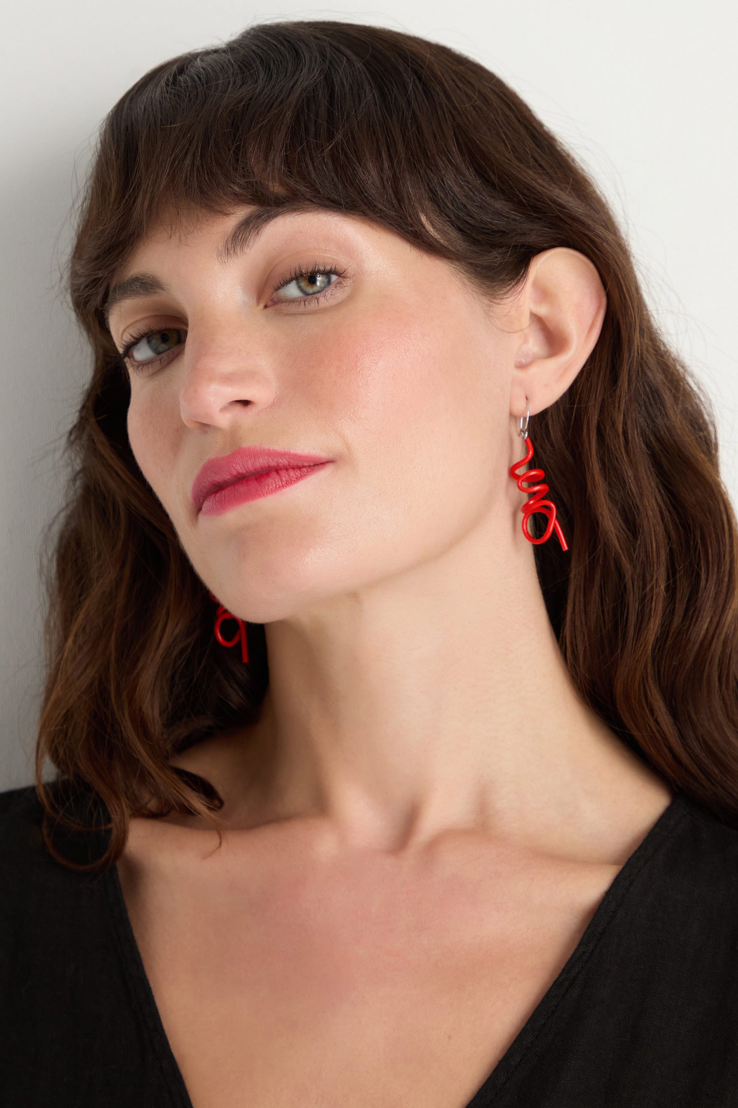 Woman with wavy brown hair and light eyes wears Mini Sketch Earrings—colourful, red spiral earrings handmade in Paris—with a black top, looking slightly to the side against a plain background.