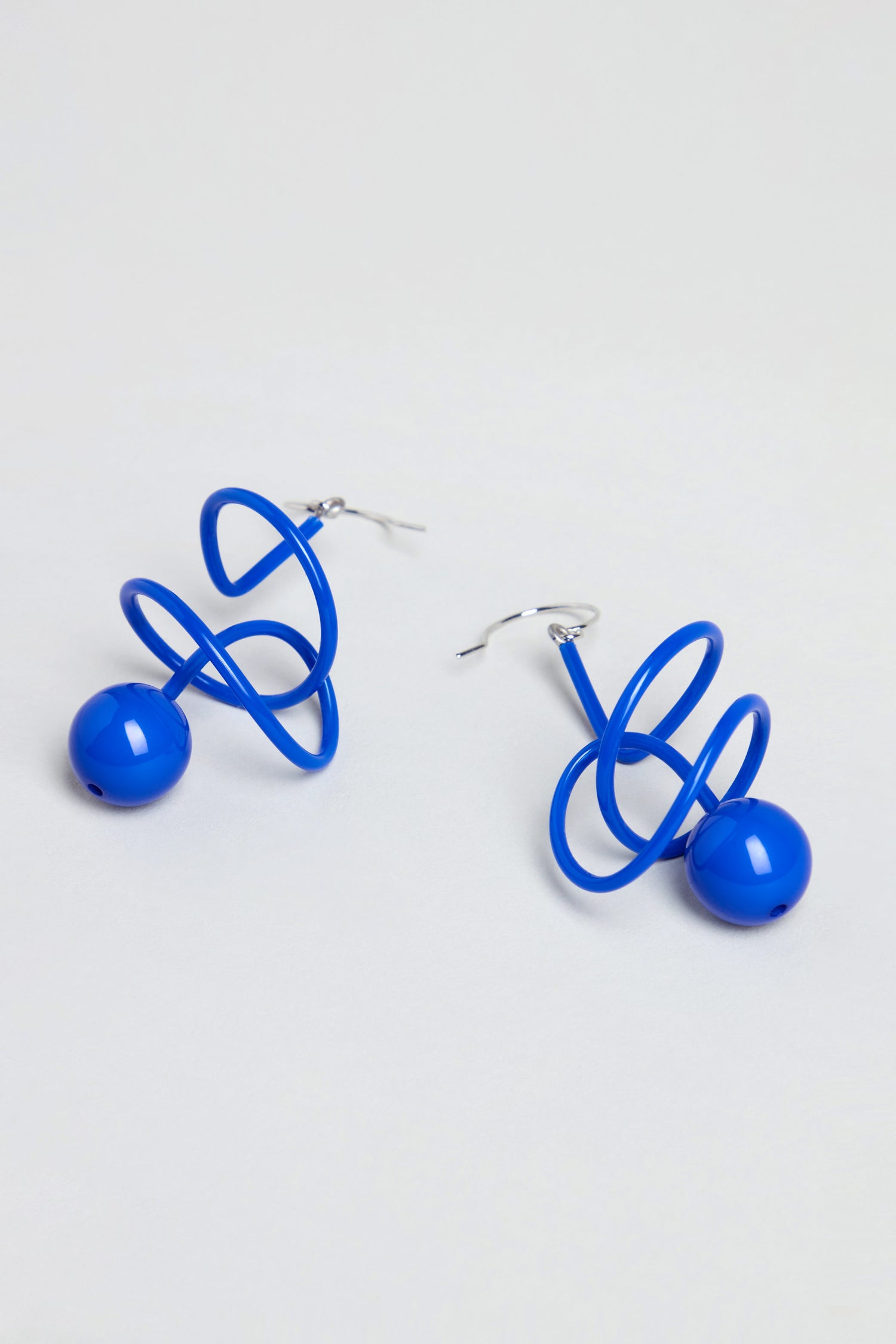 The Scribble Sphere Earrings, handmade in Paris, feature a sculptural blue spiral wire with a round bead at the base and are shown on a plain white background.