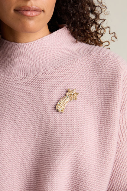 A person wearing a light pink knit sweater with the Shooting Star Brooch sparkling on the left side.